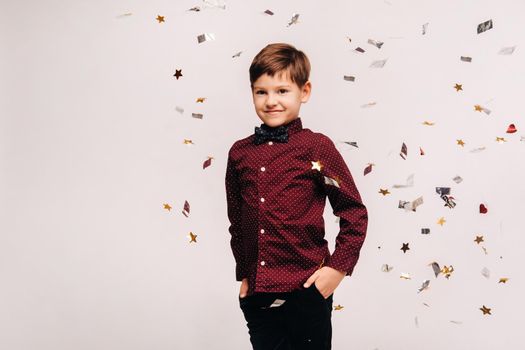 A beautiful boy stands and confetti falls on him on a gray background.