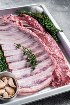 Uncooked raw rack of lamb ribs in baking dish with herbs. White background. Top view.