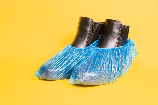 women's black leather spring boots in blue shoe covers on a yellow background copy space