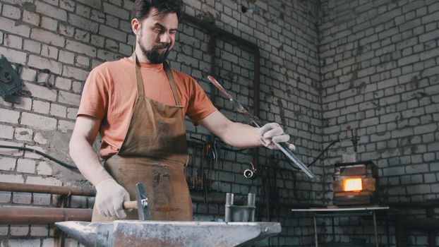 Muscular man blacksmith with hammer in forge creating steel knife, small business