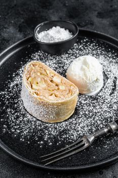 Apple strudel with cinnamon, powdered sugar and vanilla ice cream on a plate. Black background. Top view.