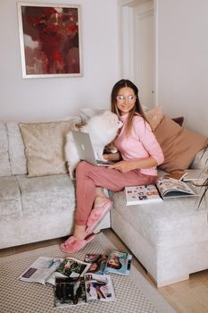 a girl in pajamas at home is working on a laptop with her dog Spitzer, the dog and its owner are resting on the couch and watching the laptop.Household chores.