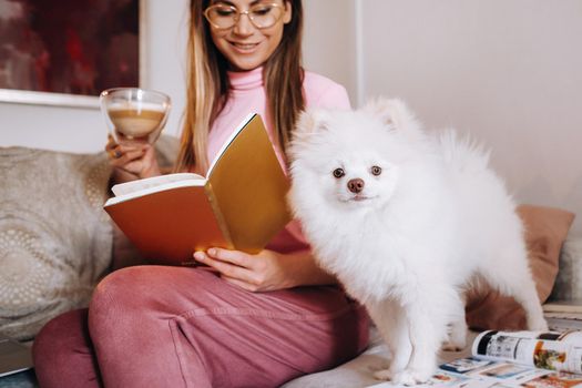 a girl in pajamas at home reads a book with her dog Spitzer, the Dog and its owner are resting on the sofa and reading a book.Household chores.