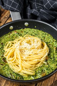Pasta spaghetti with pesto sauce and fresh spinach and parmesan in a pan. Wooden background. Top view.