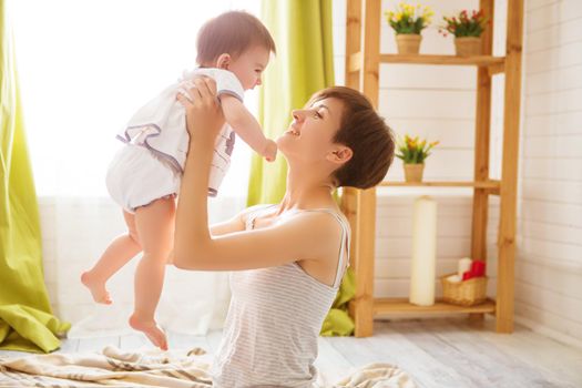 Happy mother holding her daughter high in her arms in a cozy bright room.