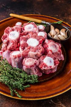 Fresh uncooked beef Oxtail cut Meat on rustic plate with herbs. Dark background. Top view.