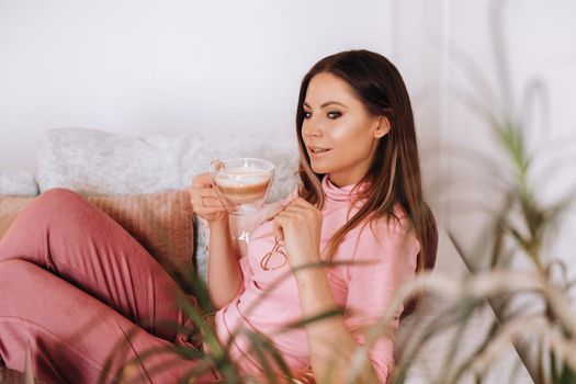 relaxed girl in the morning in pajamas at home drinking coffee .Inner peace.The girl is sitting comfortably on the sofa and drinking coffee dreaming about something.