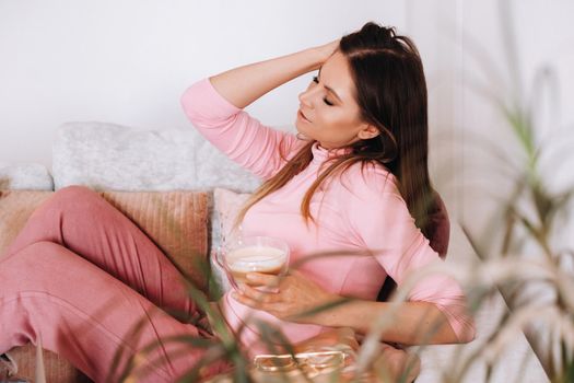 relaxed girl in the morning in pajamas at home drinking coffee .Inner peace.The girl is sitting comfortably on the sofa and drinking coffee dreaming about something.