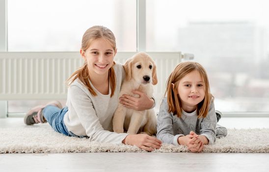 Happy friends and young golden retriever lying on floor in light room