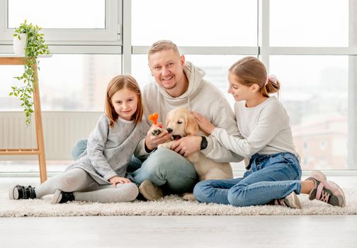 Happy family and golden retriever puppy sitting together indoors