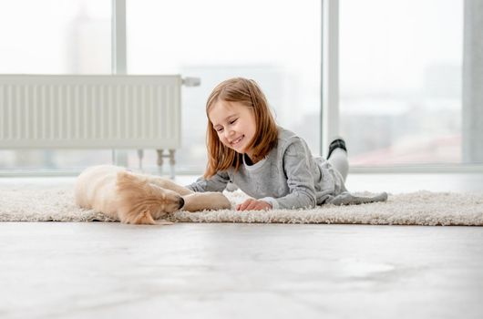 Smiling little girl with young dog golden retriever lying in light room