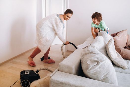 the mother vacuums the floor at home and the son watches and laughs at it.