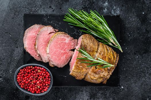 Roast beef fillet Tenderloin meat on a marble board. Black background. Top view.