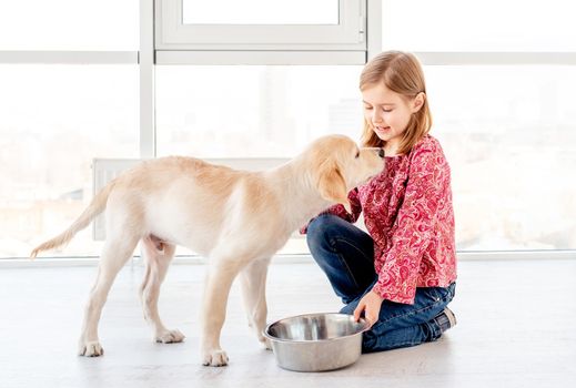 Lovely little girl giving food to her beautiful dog indoors