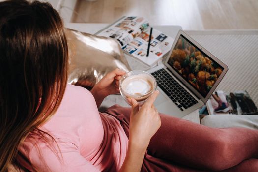 a girl in the morning in pajamas at home working on a laptop with drinking coffee, a girl self-isolated at home and resting on the couch and watching a laptop.Household chores.