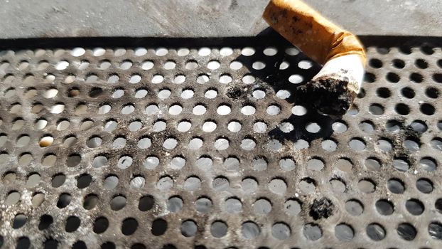 One cigarette butt on a public ashtray with a metal background.