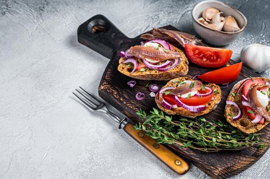 Toasts with olive oil, herbs, tomatoes and spicy anchovy fillets. White background. Top view. Copy space.