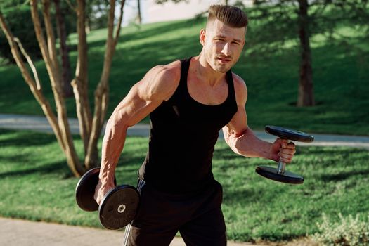 athletic man in black t-shirt with dumbbells in the park training. High quality photo