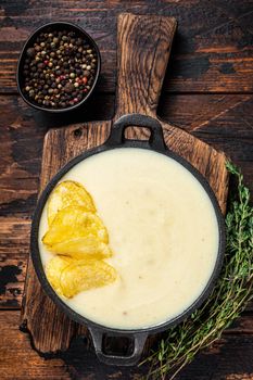 Potato cream soup with potato chips in pan on wooden board. Dark wooden background. Top view.