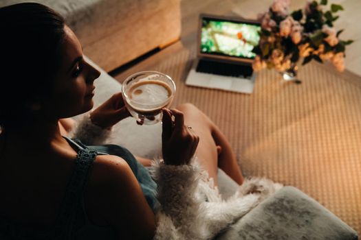 a relaxed girl at home drinks coffee and watches a movie.Domestic calm.The girl is sitting comfortably on the sofa and drinking coffee.