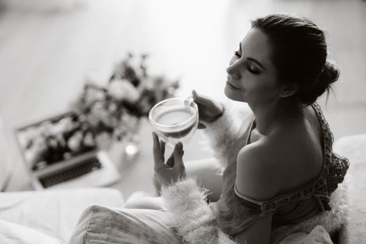 a relaxed girl at home drinks coffee and watches a movie.Domestic calm.The girl is sitting comfortably on the sofa and drinking coffee.black and white photo.