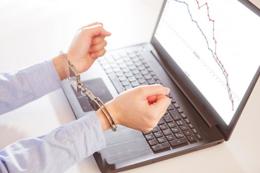 Woman hands in handcuffs with laptop with a financial graph on the screen.