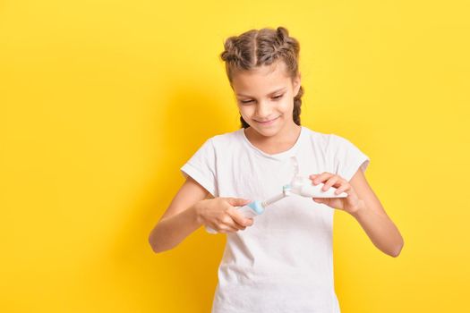 cute teenage girl with pigtails hairstyle squeezes toothpaste on an electric toothbrush, yellow background, close-up, selective focus, teen oral hygiene