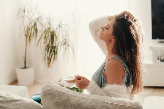 a relaxed girl at home drinks coffee and watches a movie.Domestic calm.The girl is sitting comfortably on the sofa and drinking coffee.