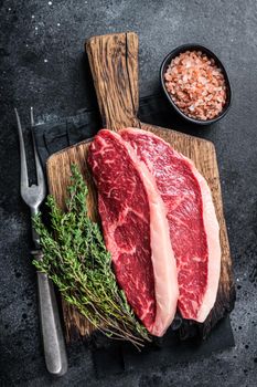 Uncooked Raw rump steak or top sirloin cap beef meat steaks on wooden board. Black background. Top view.
