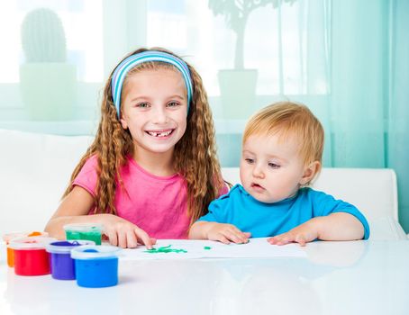 two smiling little sisters draw finger paints at home in bright living room