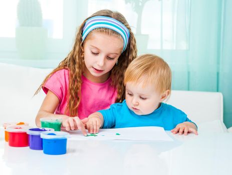 two pretty sisters draw finger paints at home in bright living room