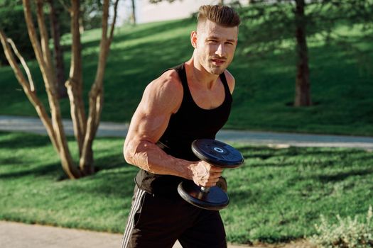 athletic man in black t-shirt with dumbbells in the park training. High quality photo