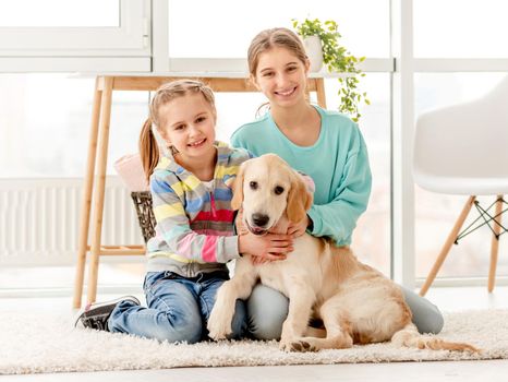 Happy sisters hugging cute young dog sitting at home