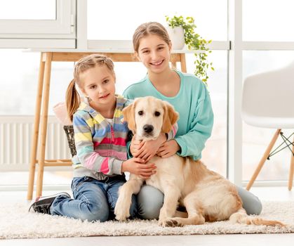 Happy sisters cuddling cute dog sitting on floor at home