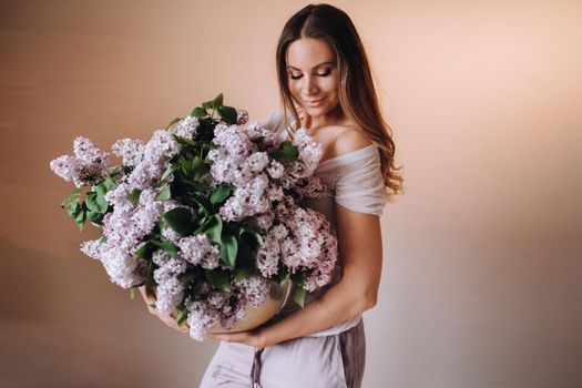 Beautiful girl with lilac flowers in her hands. A girl with lilac flowers in the spring at home. A girl with long hair and lilac in her hands.