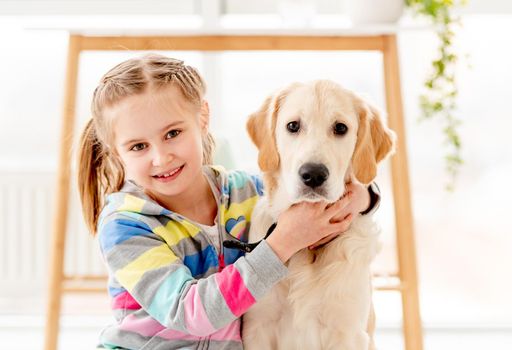 Beautiful little girl hugging cute young dog indoors