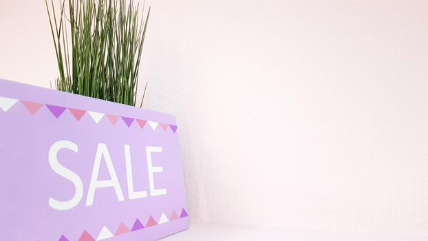 sign on a shelf with the inscription discount on a background of a pale pink wall with a green plant in a women's clothing store. selling nameplates. Discount at the boutique of the shopping center