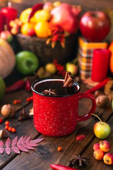 red mug with mulled wine. Cinnamon sticks stick out of the cup and a star of star anise floats. Fruits and spices are all around on a table