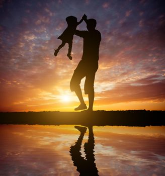 Dad playing with baby daughter on the beach at sunset. Silhouette photo