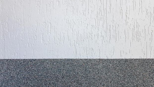 Gray marble chips and decorative light stucco on the wall divided by a horizontal line. Building facade background. Stucco texture on the street.