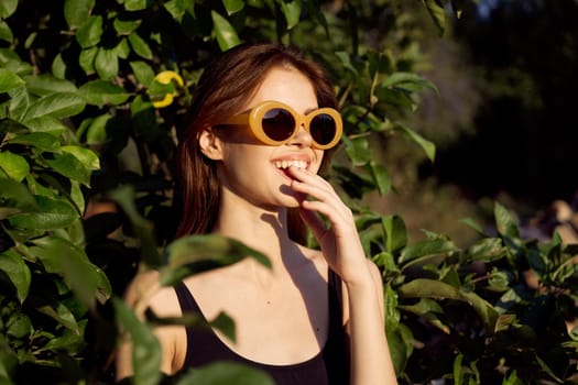 cheerful woman wearing sunglasses green leaves nature summer posing. High quality photo