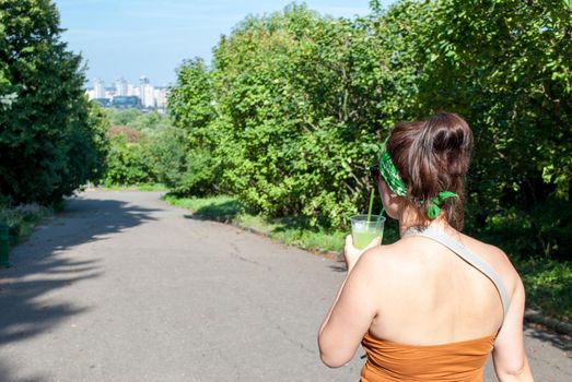 Young beautiful girl drinking a green drink from a plastic cup takeaway food. Summer cold drinks.