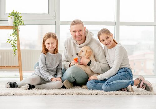 Happy family and golden retriever puppy sitting together indoors