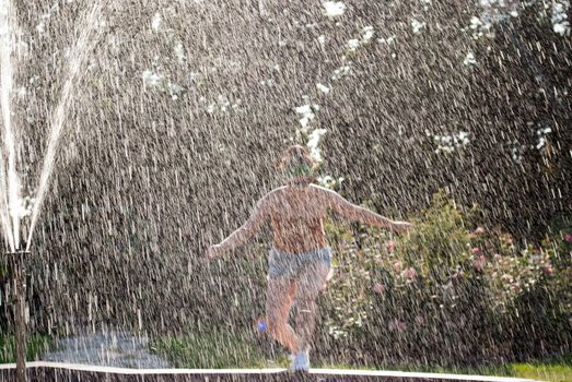 happy girl runs through a fountain in a green park in the sunshine.