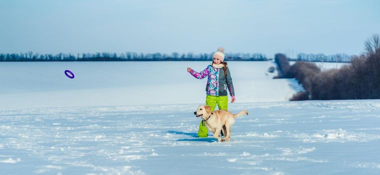 Smiling girl throwing toy ring to playful dog on winter field