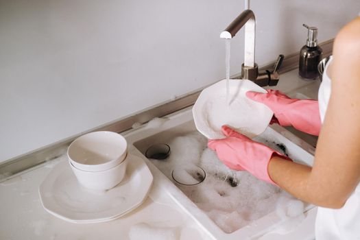 housewife girl in pink gloves washes dishes by hand in the sink with detergent. The girl cleans the house and washes dishes in gloves at home