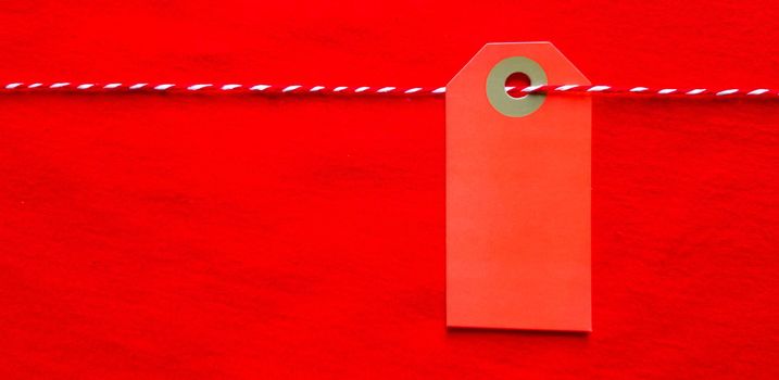 Red tag tag hanging on a red rope on a red background. Copy space, place for text, flat lay