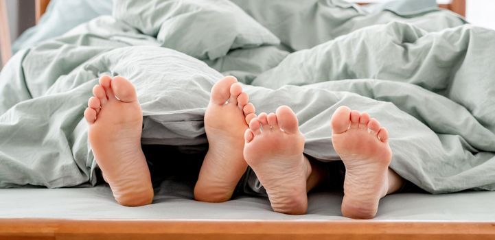 Feet of couple in the bed under the blanket. Legs og man and woman together in the bedroom in the morning. Concept of rest, love and happy family relationships