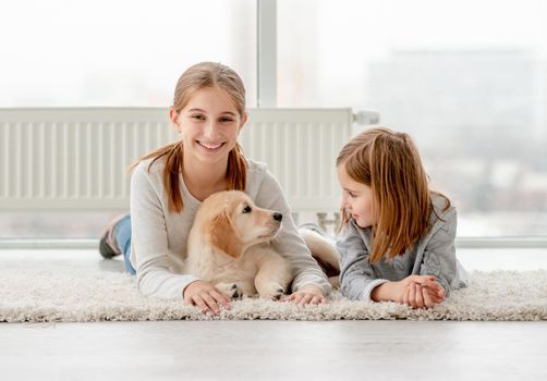 Happy friends and young golden retriever lying on floor in light room