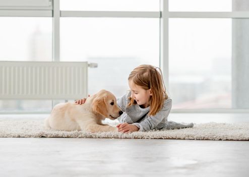 Smiling little girl with young dog golden retriever lying in light room